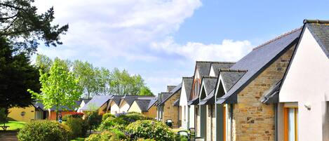 A row of cottages with stone walls and pitched roofs, a paved pathway, and outdoor seating areas.