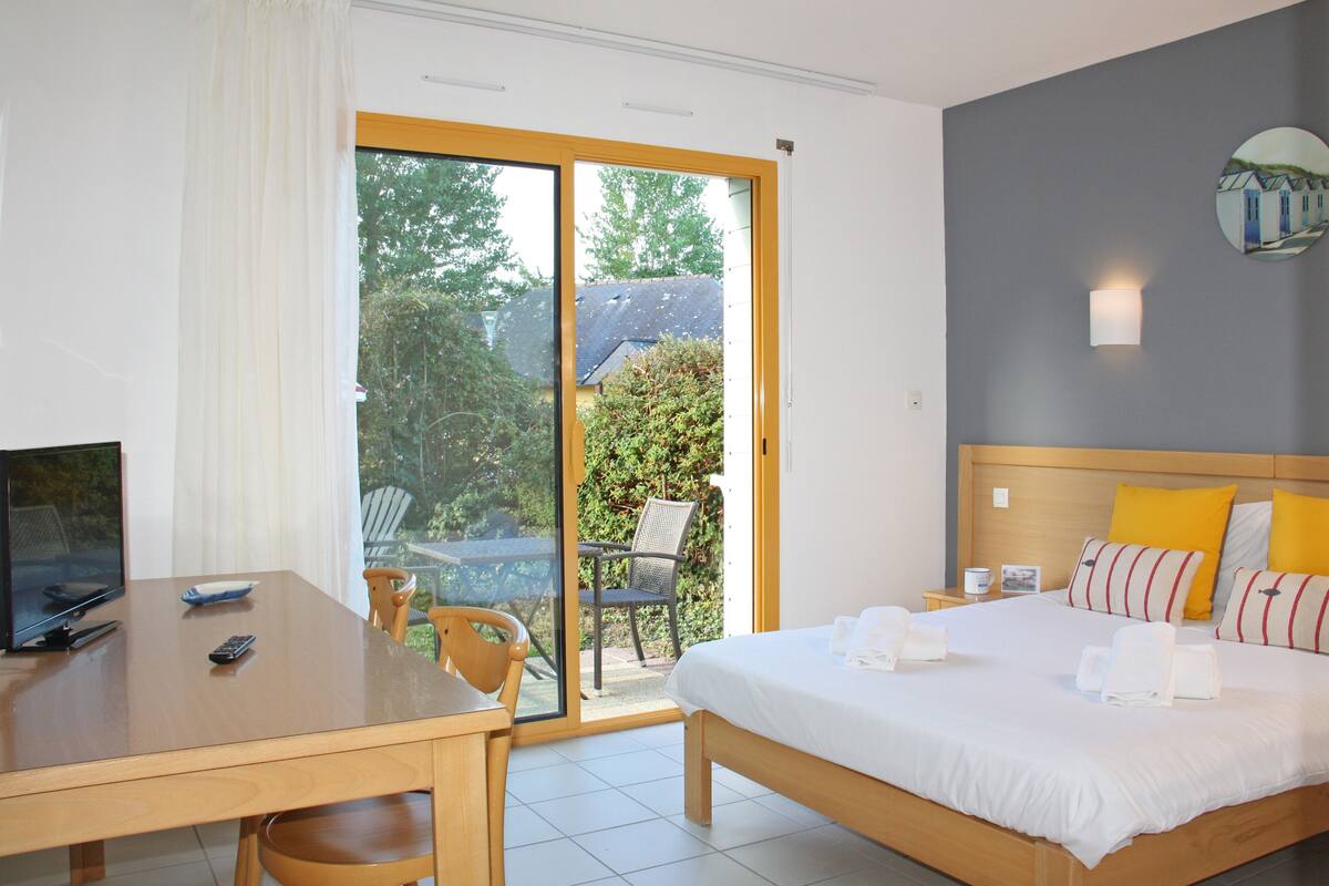 A hotel room with a bed, a desk with a computer, a chair, and a view of the outdoors.