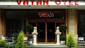 The entrance of Vatan Hotel with a prominent sign, a glass door, and symmetrical landscaping with potted plants and a bench. - Vatan Hotel (Izmir)