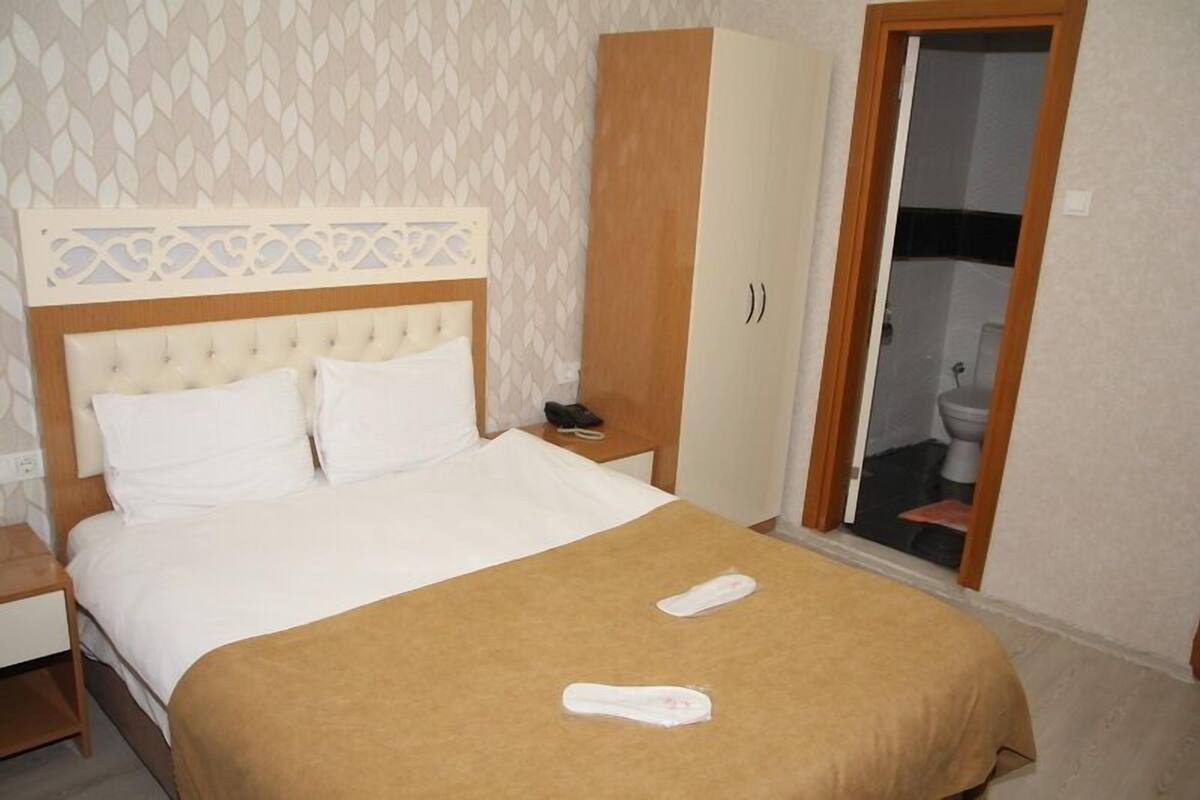 A hotel room with a bed, a wardrobe, a nightstand, and a bathroom visible through an open door.