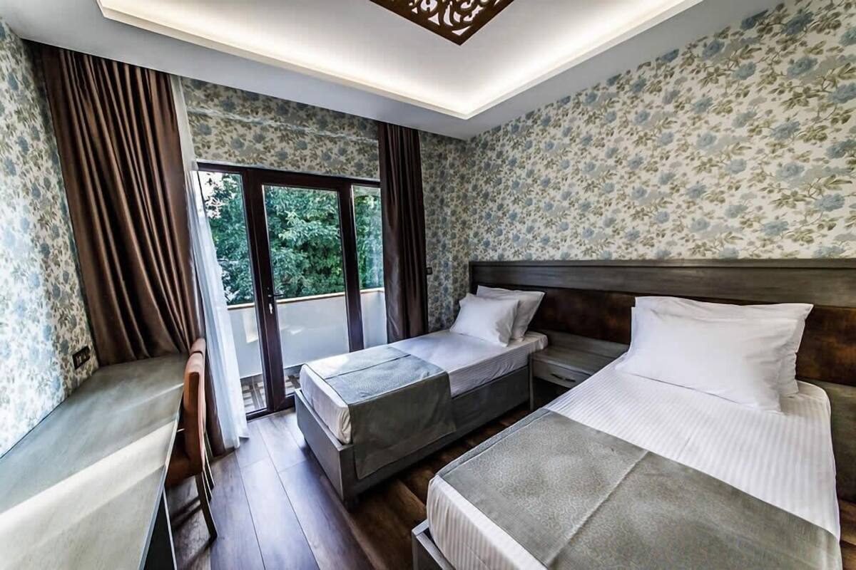 Een slaapkamer met twee bedden, een bureau en uitzicht op groen door een groot raam.