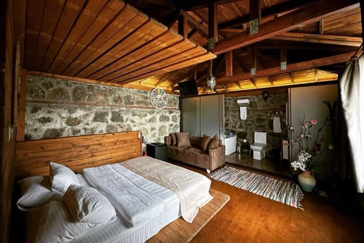 Een knus slaapkamer met een houten plafond, een stenen muur, een bed met witte lakens, een bruine bank en een kleine tafel.