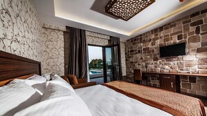 A hotel room with a large bed, a stone wall, a flat-screen TV, and a view of the outdoors. - My Green Otel (Kartepe)