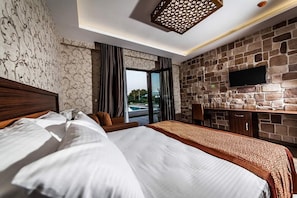 Een hotelkamer met een groot bed, een stenen muur, een flatscreen televisie en uitzicht op het omliggende landschap.
