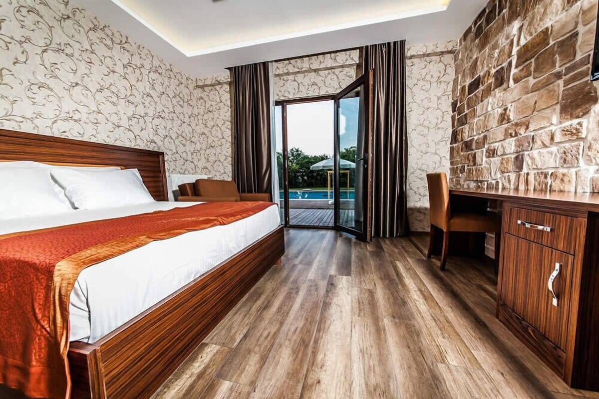 Een hotelkamer met een groot bed, een bureau en uitzicht op een zwembad door een glazen deur.