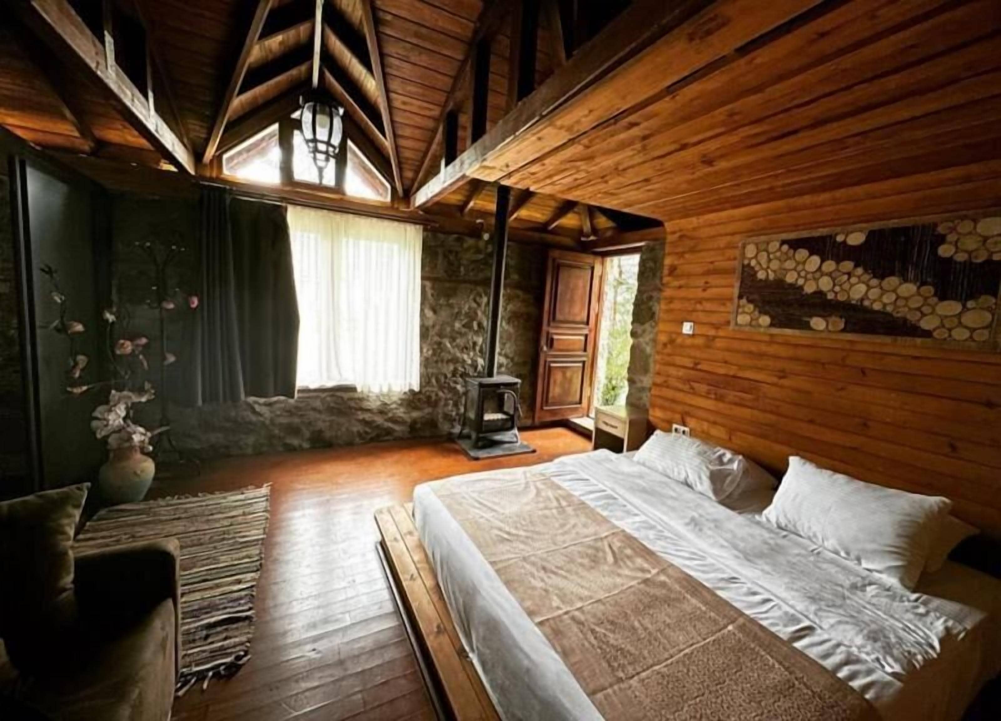 A rustic wooden room with a bed, a fireplace, and a stone wall.