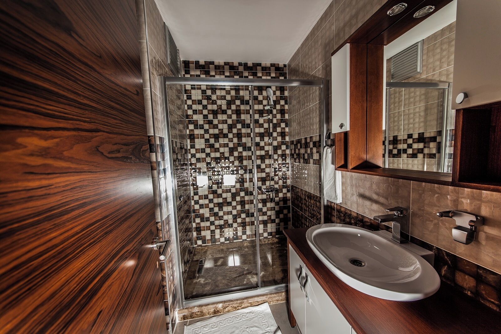 A modern bathroom with a glass shower enclosure, a white sink, and a wooden vanity.