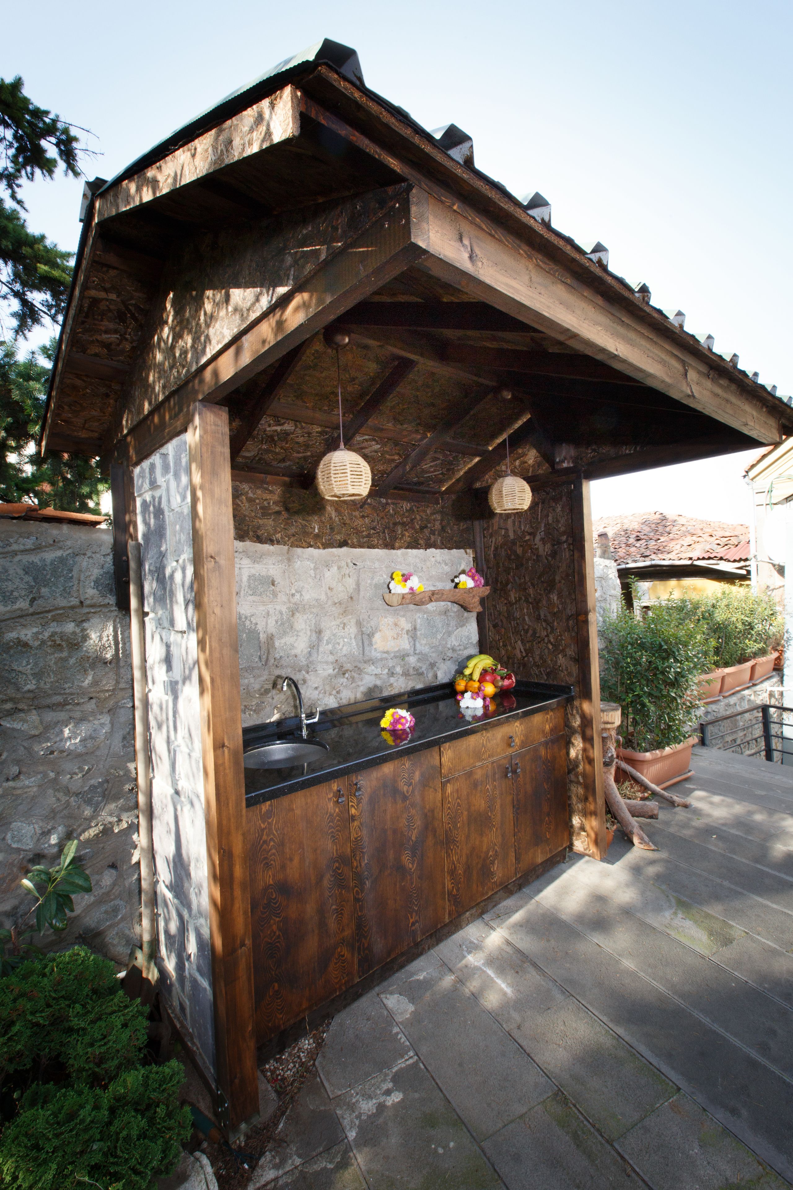 A rustic outdoor kitchen with a stone wall, wooden counter, and hanging lanterns.