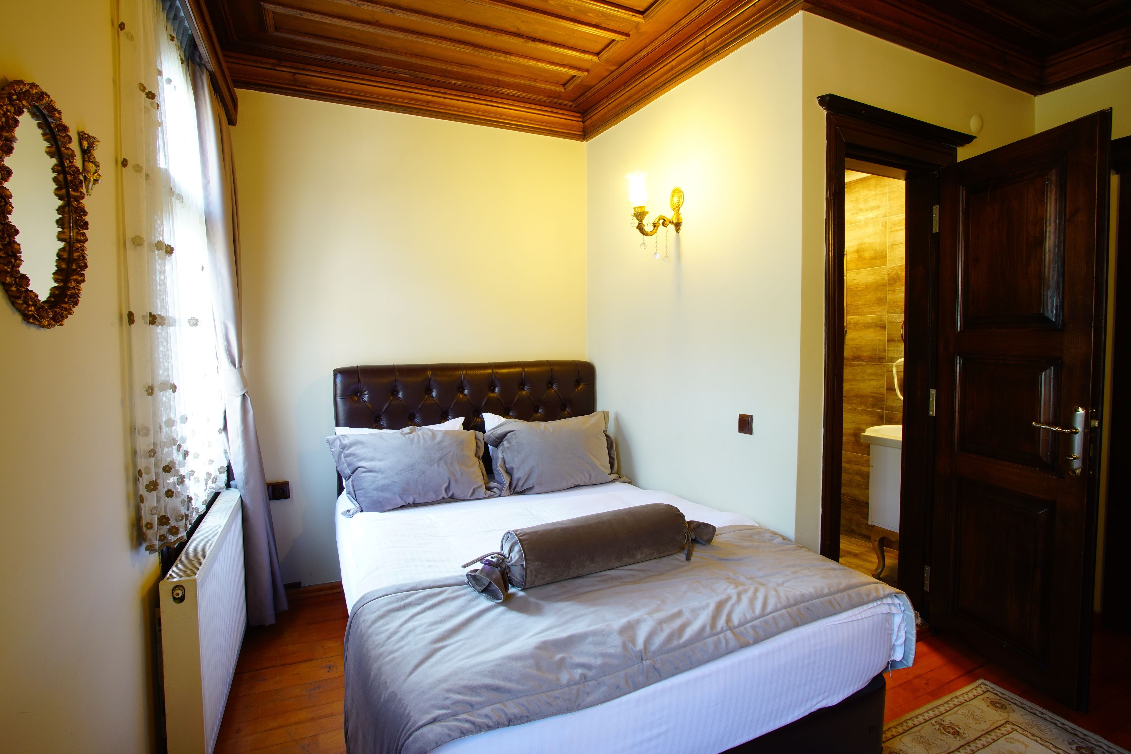Un dormitorio con cabecera de madera, una cama con un edredón doblado, una lámpara de pared y una puerta que da al baño.