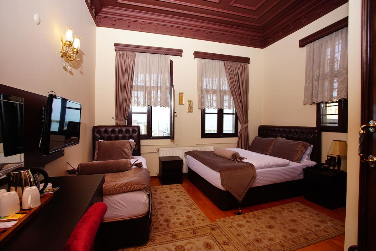 Ein Hotelzimmer mit einem großen Bett, einem Schreibtisch mit Fernseher und zwei Fenstern mit Vorhängen.