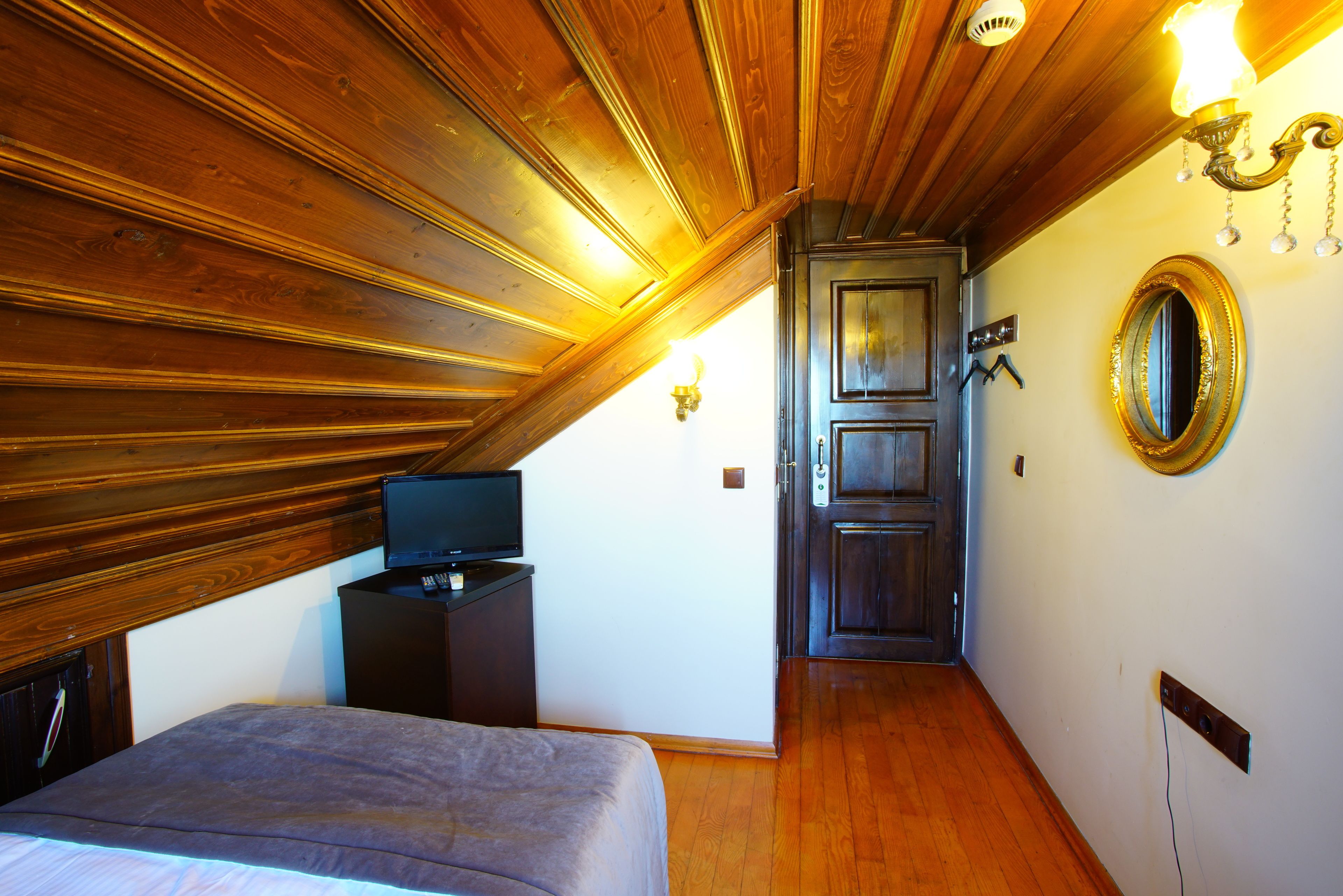 A bedroom with a wooden ceiling, a bed, a television on a dresser, and a door leading to another room.