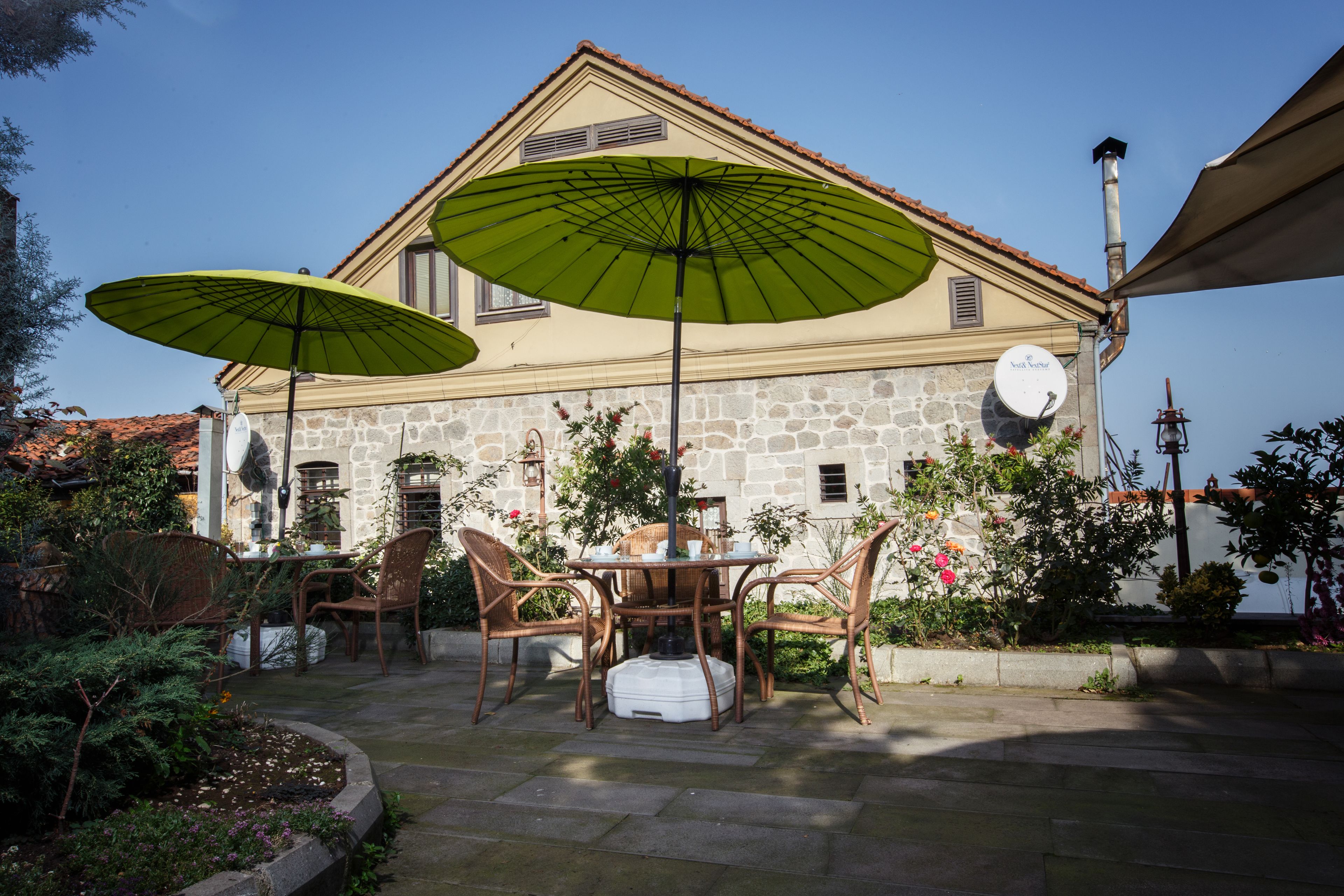 A stone building with a tiled roof, a table with chairs, and two green umbrellas.