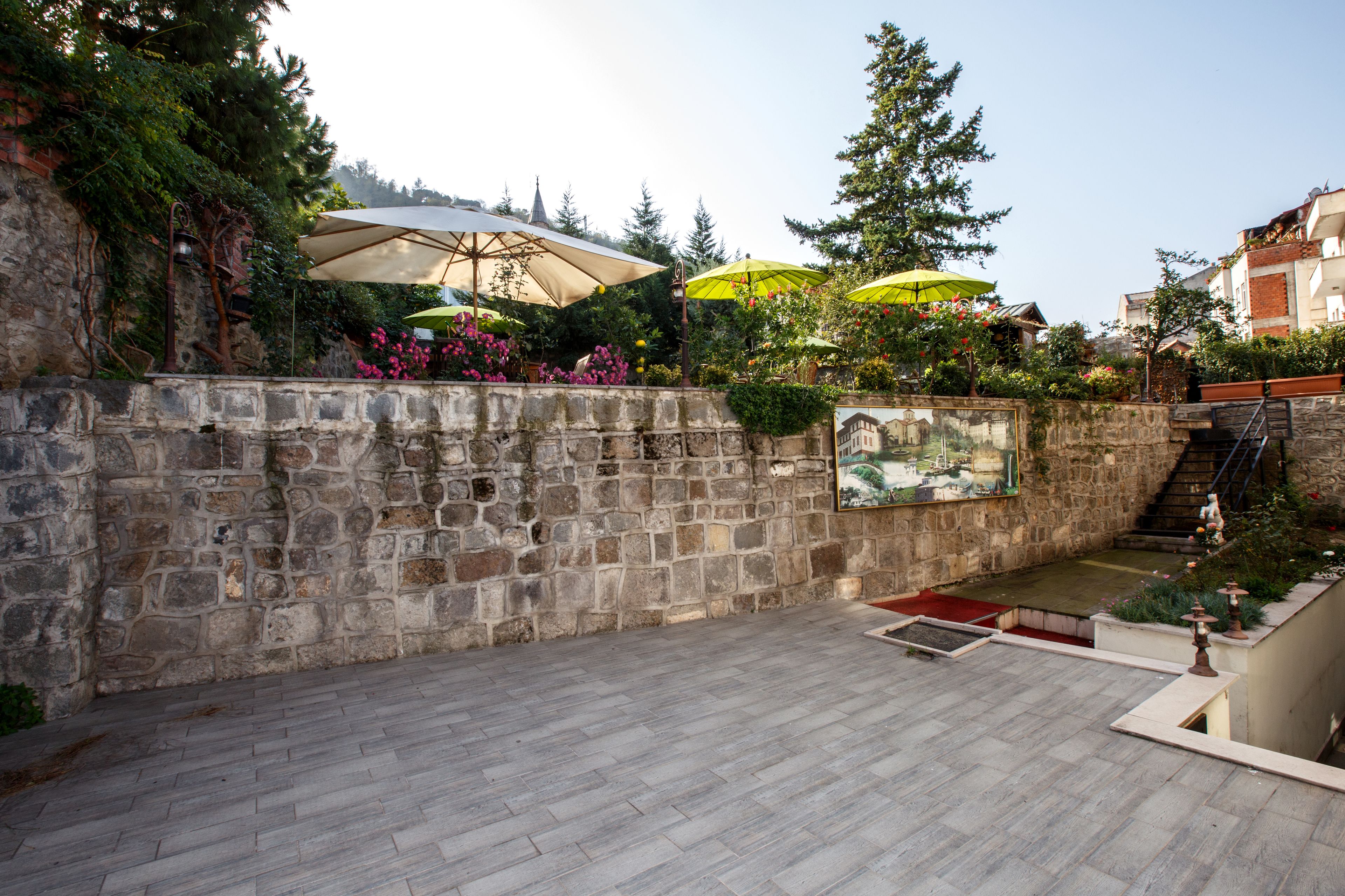 Un muro de piedra con un mural, zona de estar al aire libre con sombrillas y una escalera que lleva a un nivel superior.