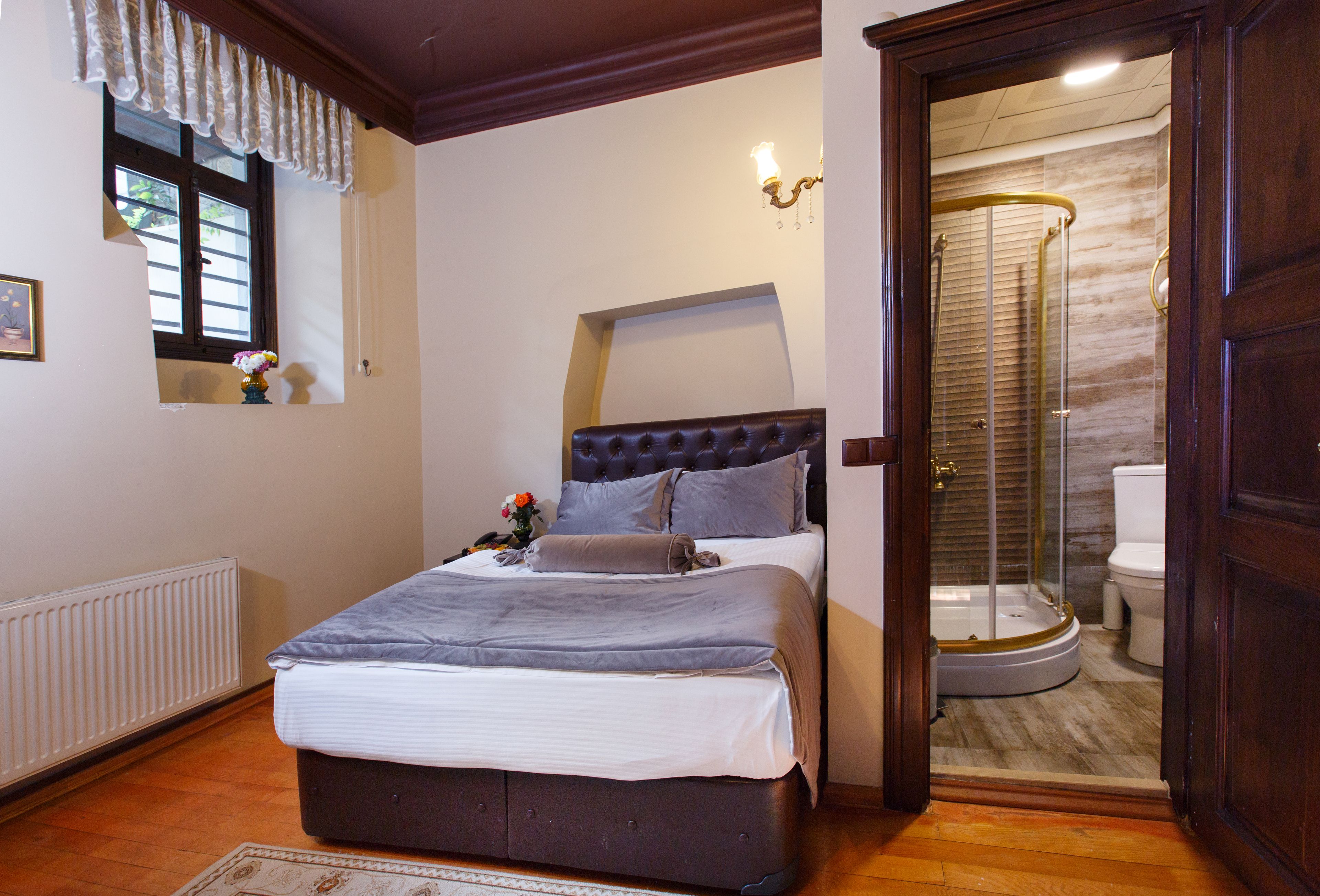 A bedroom with a bed, a window with curtains, a radiator, and a shower area.