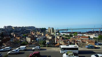 A cityscape with a view of the sea, featuring a mix of residential and commercial buildings, a bridge, and a parking lot with various vehicles.