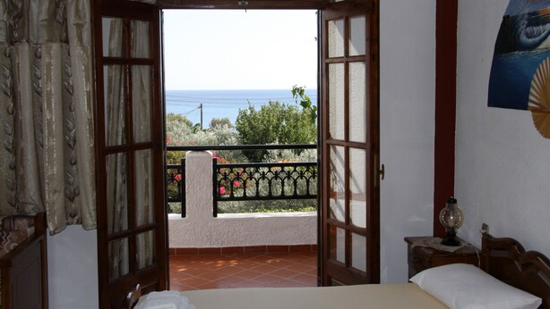 Une chambre avec un lit, une table de chevet et une vue sur la mer, visible par une porte ouverte.