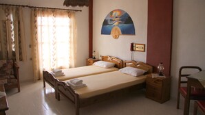 Une chambre avec deux lits, une chaise en bois, une table et une lampe fixée au mur.