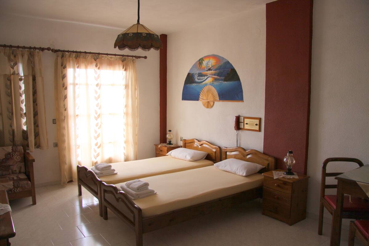Une chambre avec deux lits, une chaise en bois, une table et une lampe fixée au mur.
