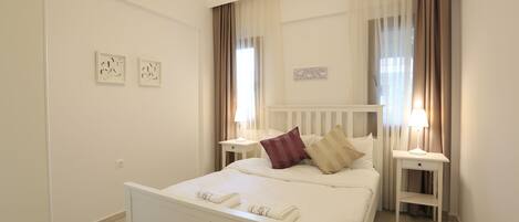 A neatly arranged bedroom with a bed, bedside tables, and a nightstand.