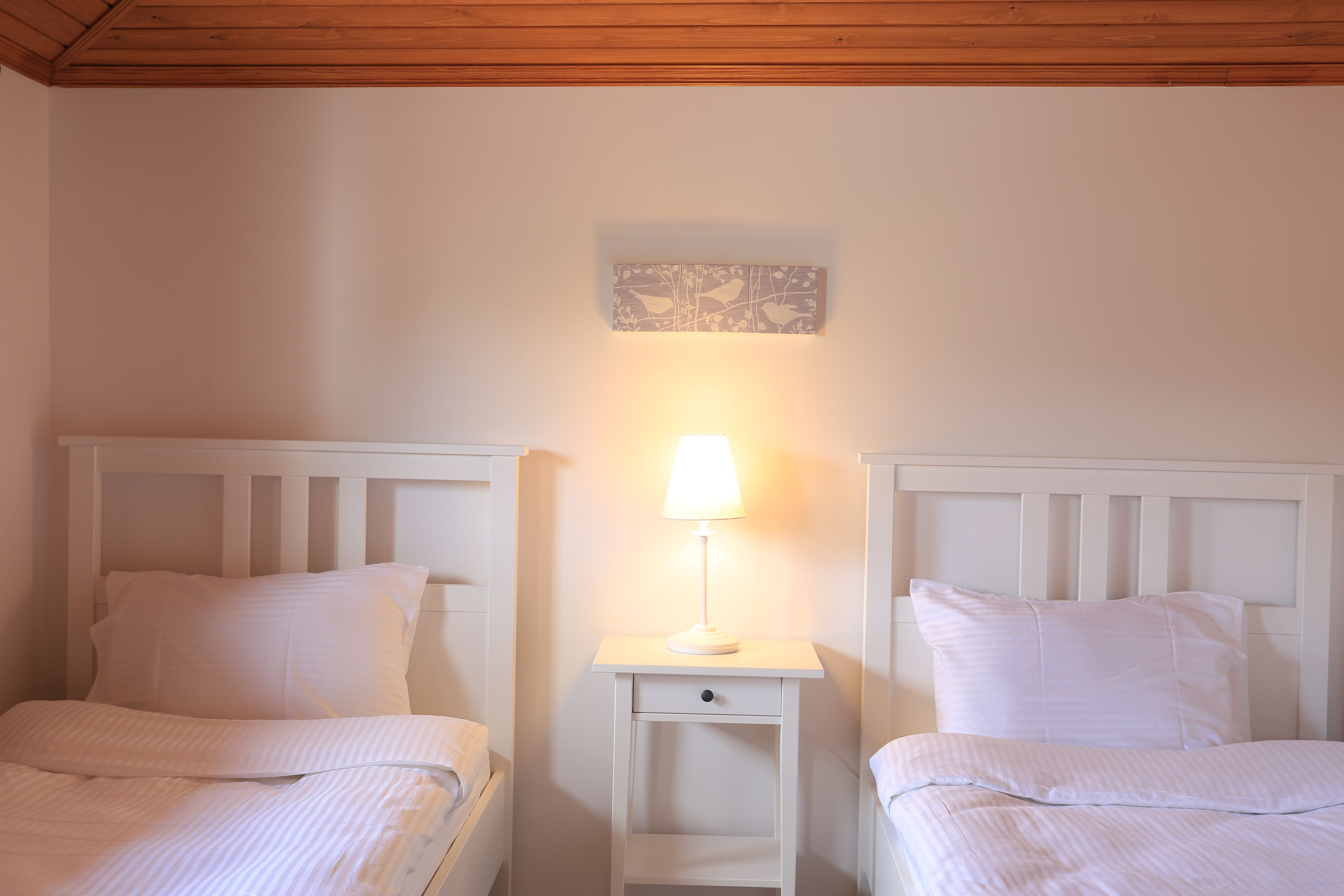 Un dormitorio con dos camas, una mesita de noche con lámpara y una obra de arte colgada en la pared.
