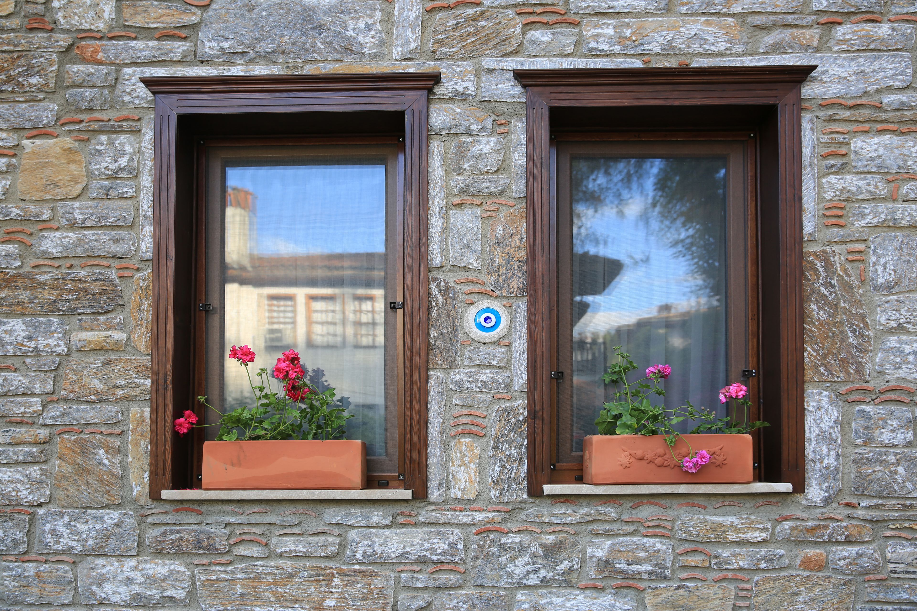 Dos ventanas con marcos marrones y jardineras con flores rosadas.