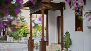 A covered outdoor area with a stone wall, wooden pillars, and a staircase leading to a door. - Alp Suites Lavanta (Ula)