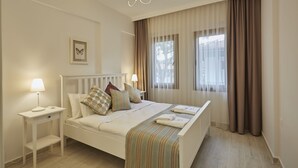 A neatly arranged bedroom with a bed, bedside tables, a lamp, and a window with curtains. - Alp Suites Lavanta (Ula)
