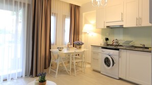 A modern kitchen with a washing machine, a dining table with chairs, and a chandelier. - Alp Suites Lavanta (Ula)