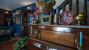 A room with a piano, a blue sofa, a decorative cabinet with a mirror, and a staircase.