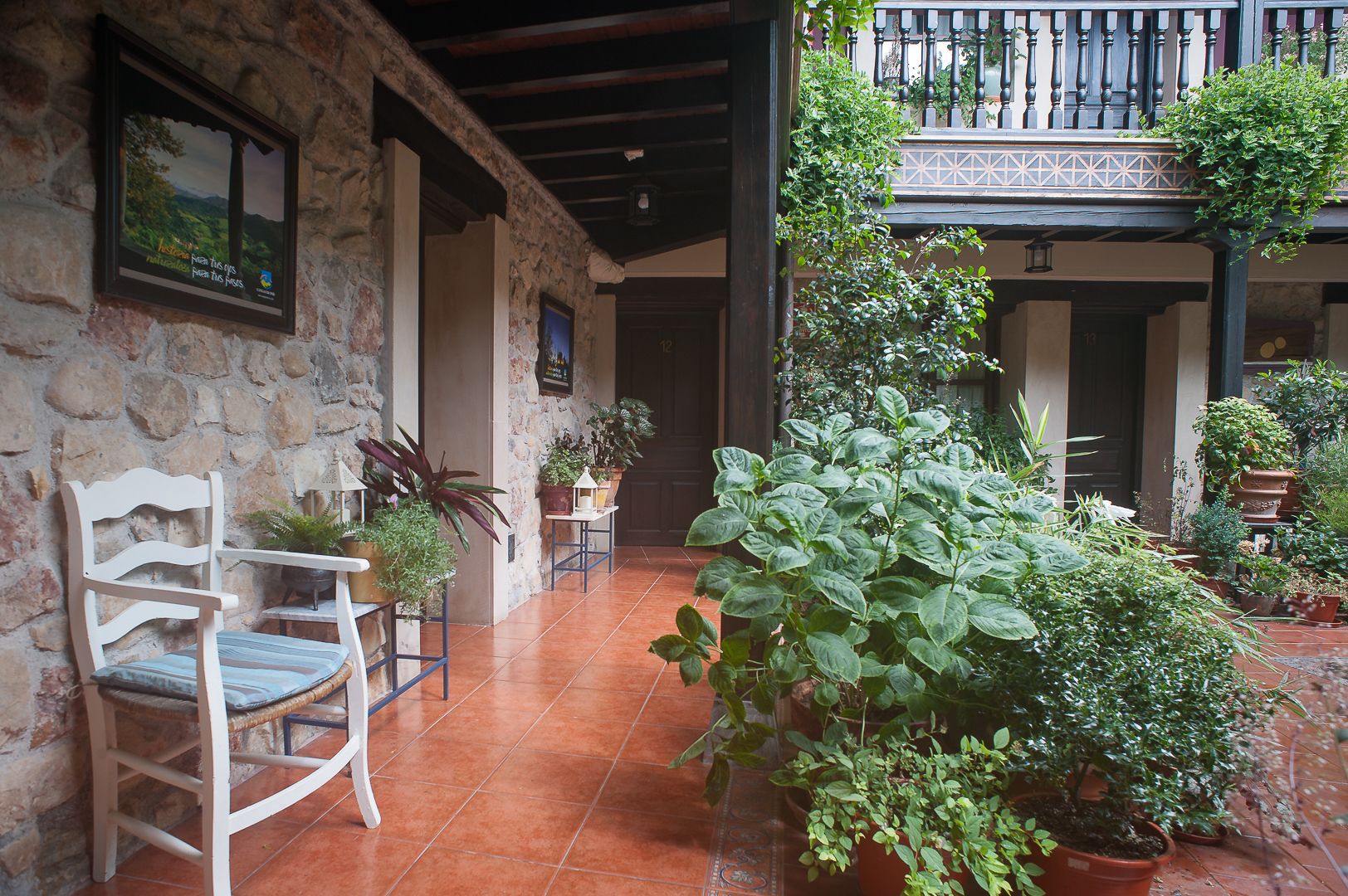 A stone-walled courtyard with a wooden chair, potted plants, and a balcony with a railing.