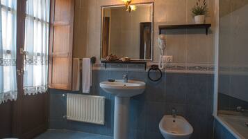 A bathroom with a pedestal sink, a bidet, a towel rack, a mirror, and a shelf with a plant.