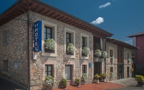 Edifici de pedra amb un cartell que indica que és un hotel. Hi ha plantes en testos a la planta baixa i cistelles florals penjants a les finestres.
