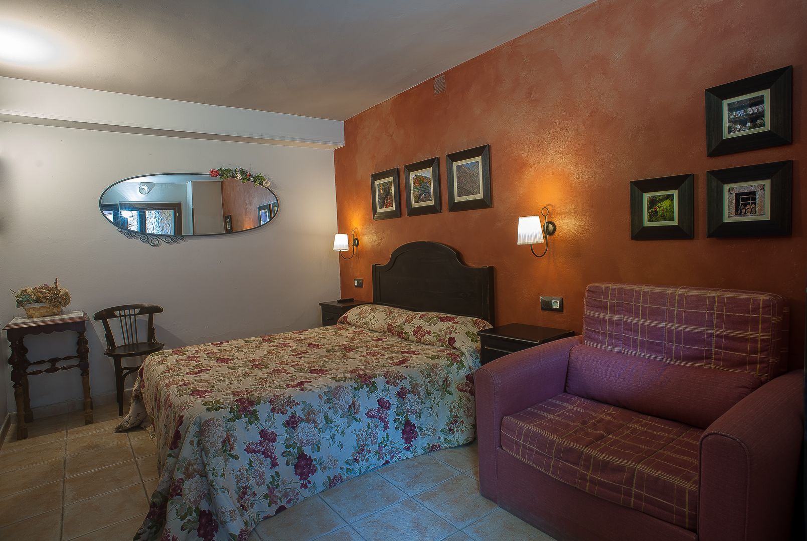 A bedroom with a bed, a chair, a nightstand, a mirror, and wall-mounted lights.
