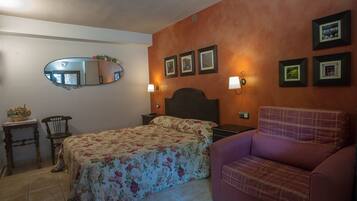 A bedroom with a bed, a chair, a nightstand, a mirror, and wall-mounted lights.
