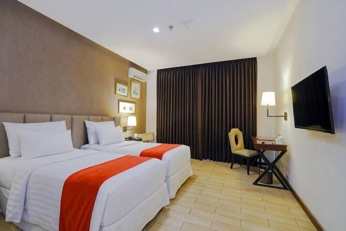 Habitación de hotel con dos camas, un escritorio, una silla, un televisor y una ventana con cortinas.