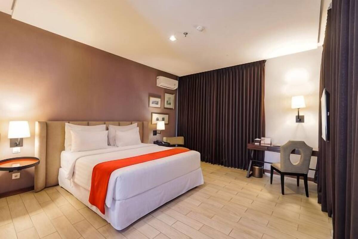 Una habitación de hotel con una cama, mesitas de noche, un escritorio y una silla.