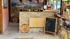 A reception area with a stone wall, a wooden reception desk, a chalkboard menu, and a mural of hot air balloons. - Sinter Terasse House Hotel (Denizli)
