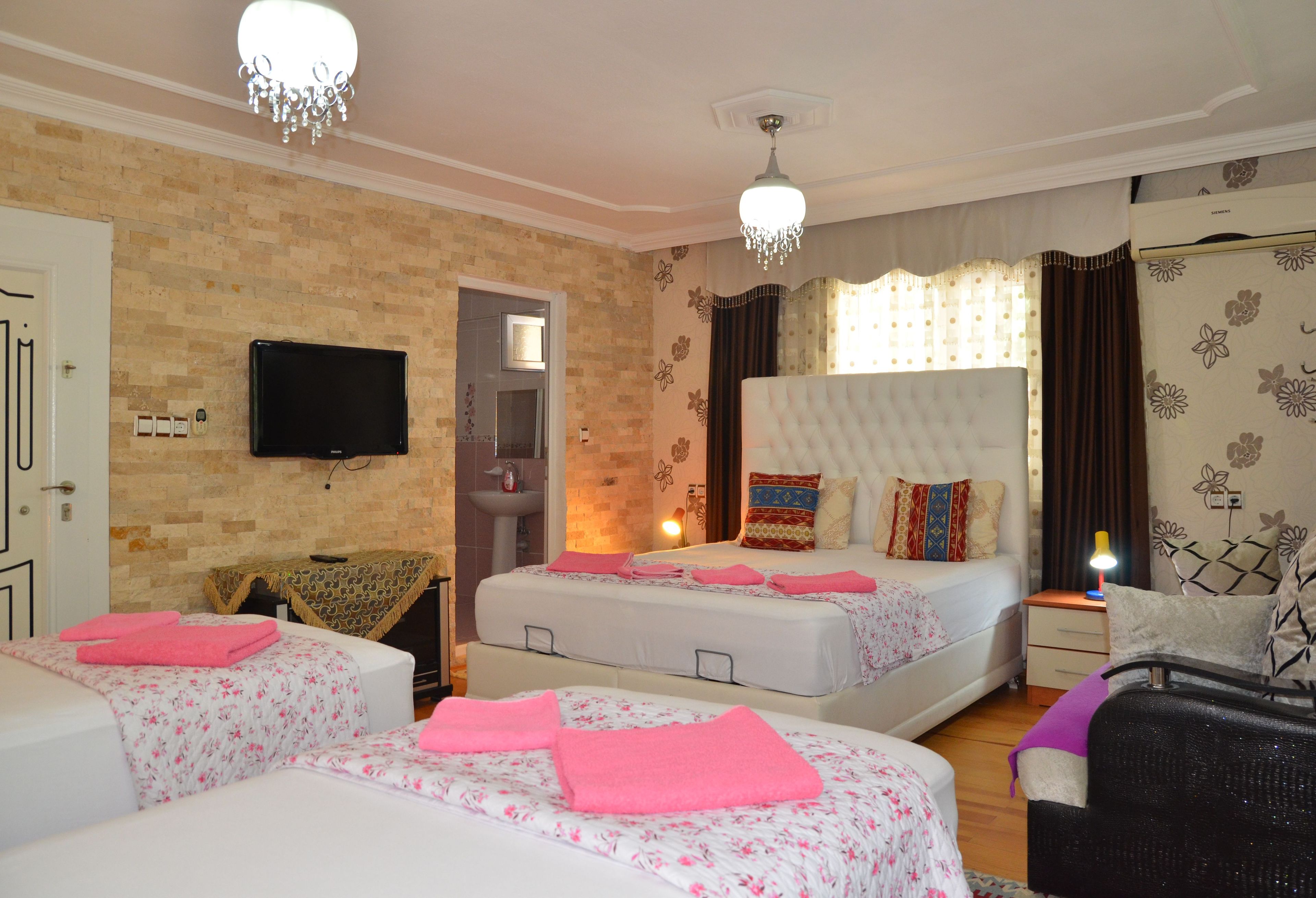 A hotel room with two beds, a TV, a chandelier, and a bathroom visible through an open door.