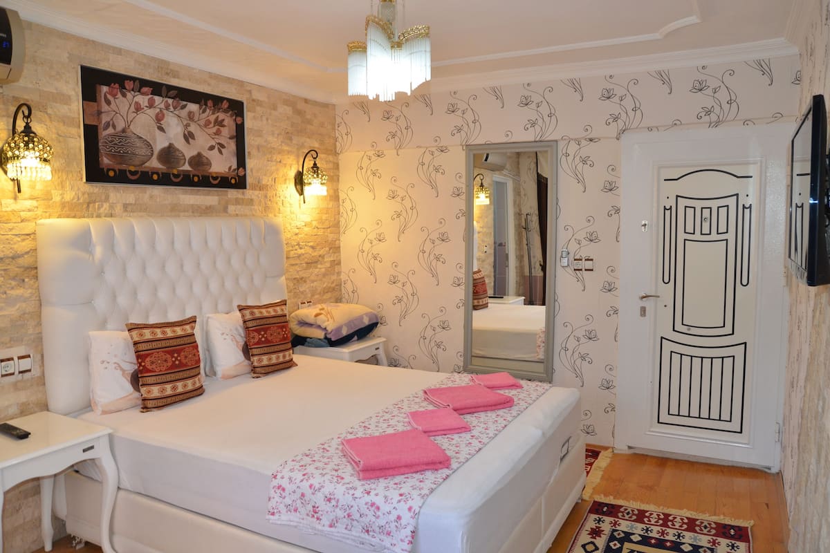 A bedroom with a tufted headboard, a large mirror, and a patterned wall.