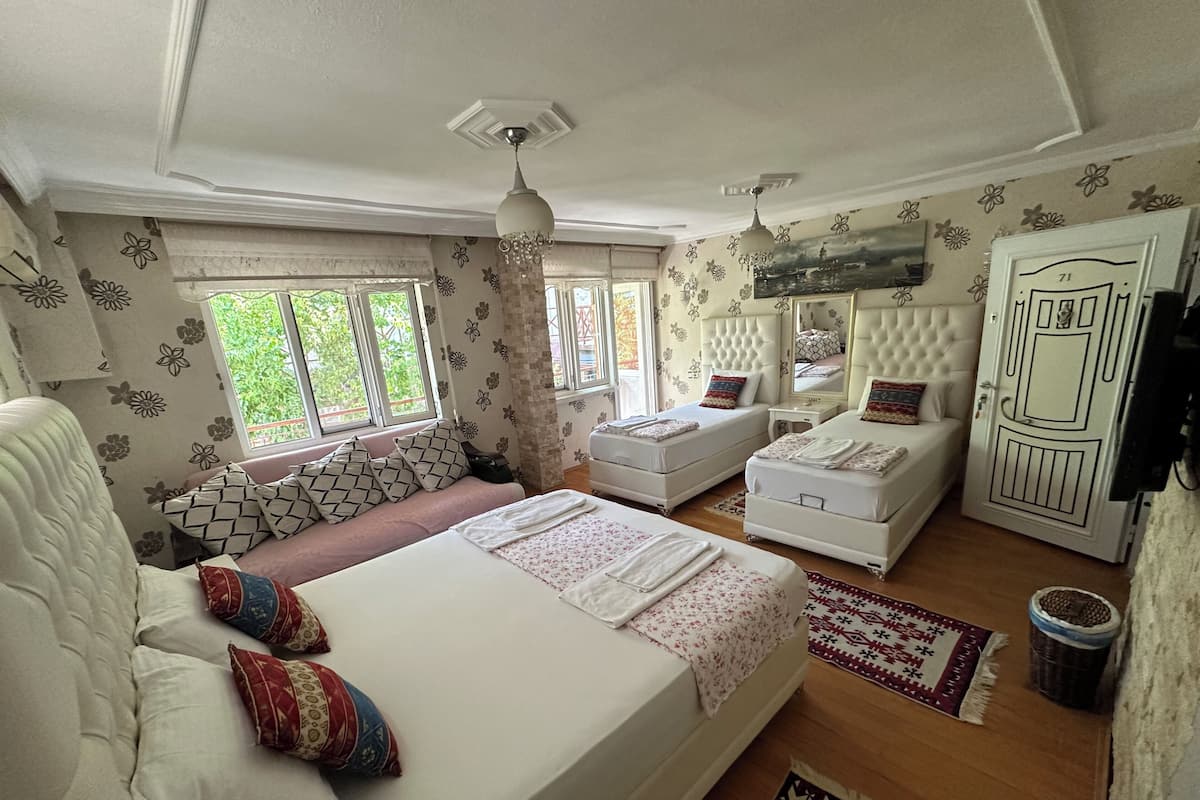 A well-lit bedroom with a large bed, two white sofas, a small table, and a wardrobe.
