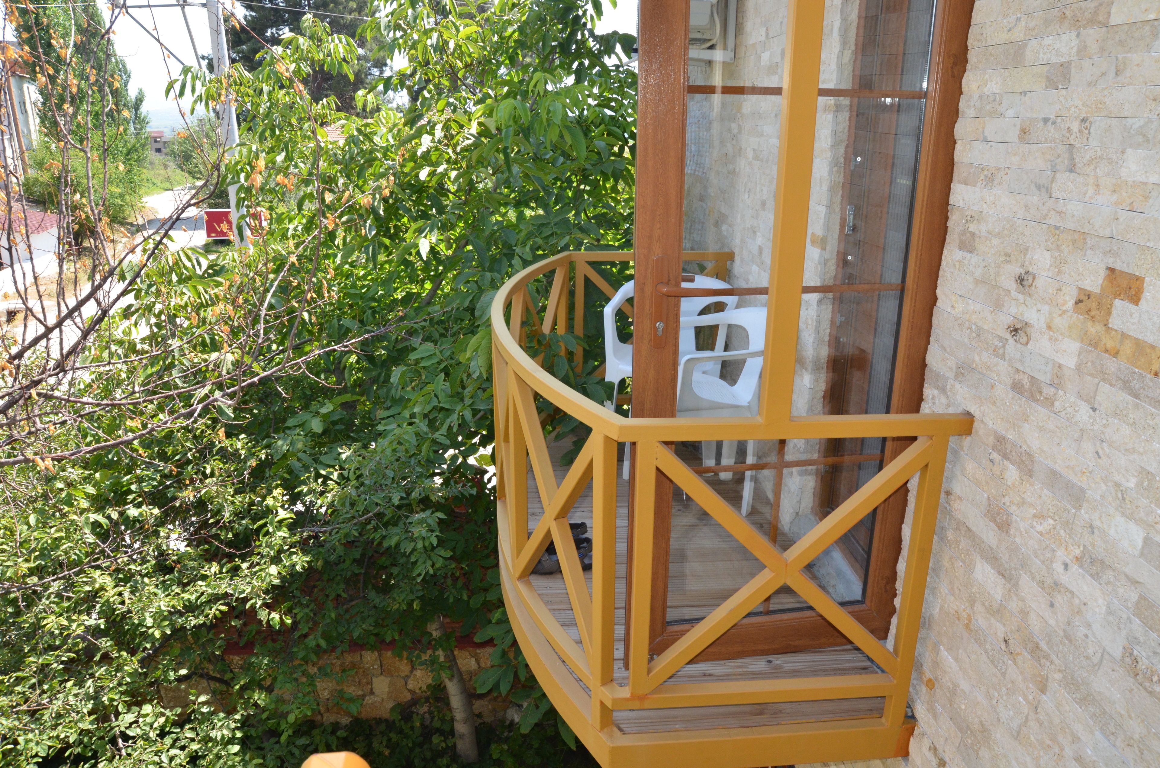 Un balcon en bois avec une porte vitrée, entouré de verdure.