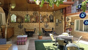 A cozy outdoor seating area with wooden tables and chairs, surrounded by stone walls and decorative elements. - Sinter Terasse House Hotel (Denizli)