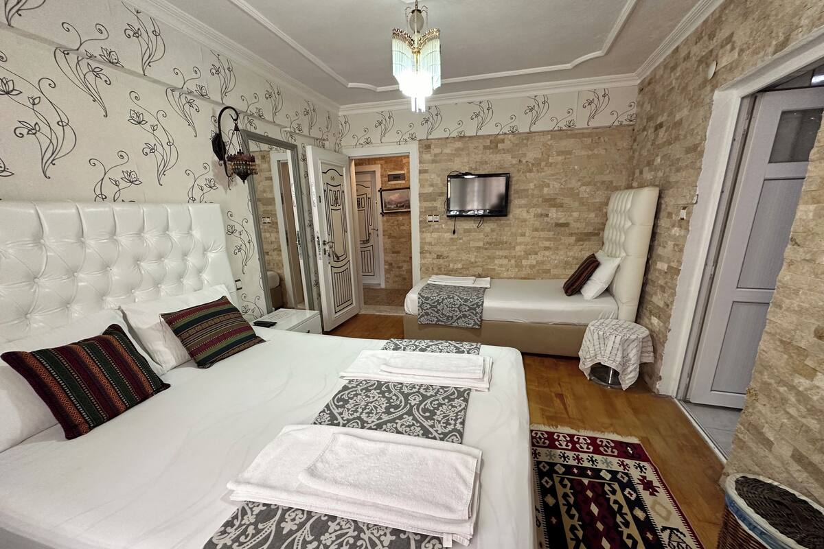 A hotel room with a large bed, a smaller bed, a TV, and a bathroom visible through an open door.