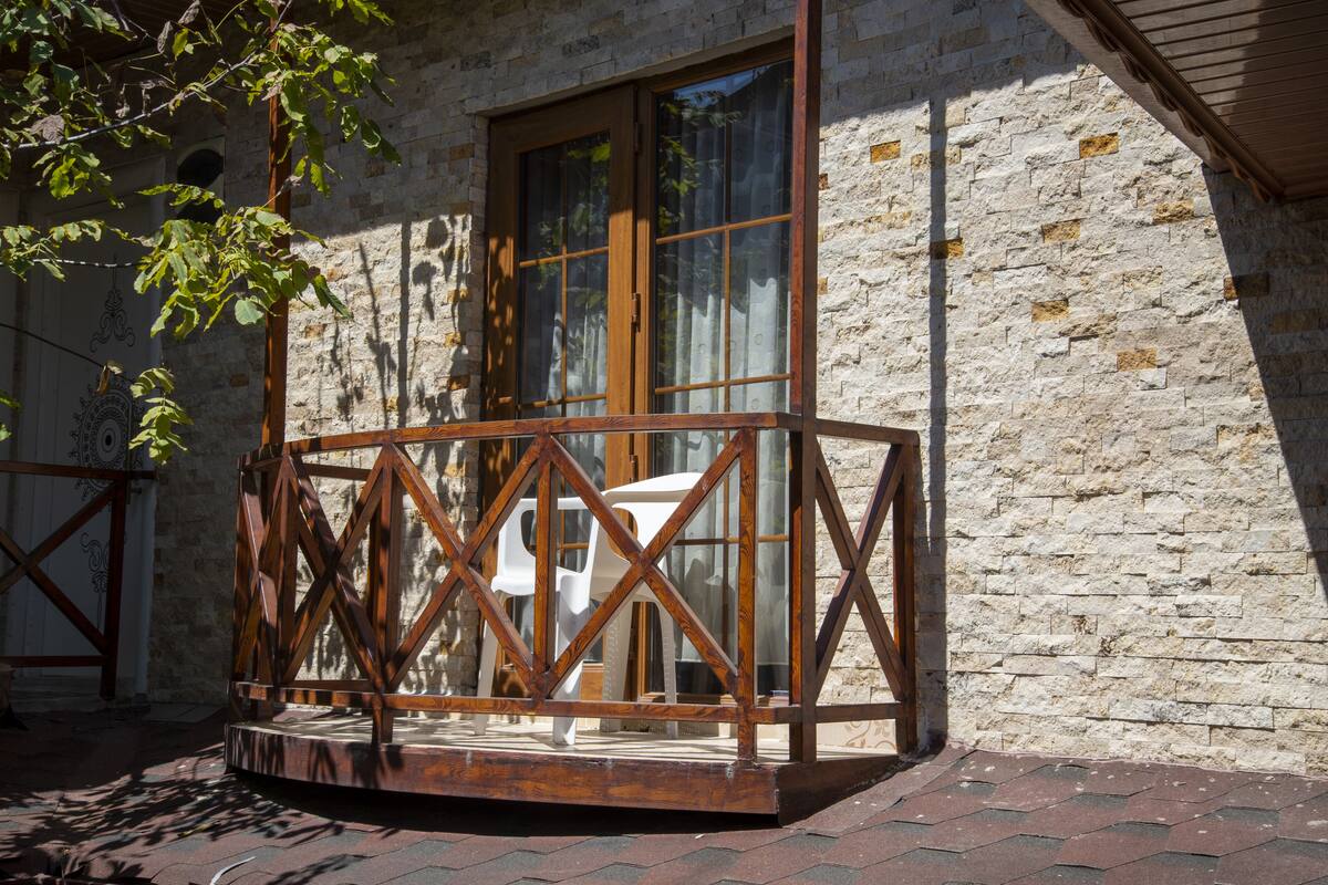 A wooden balcony with a geometric railing, a white chair, and a stone wall.