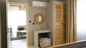 A hallway with a white air conditioning unit, a round mirror, a wooden door, and a small white sink with a patterned towel. - Alp Suites Mandalin (Ula)