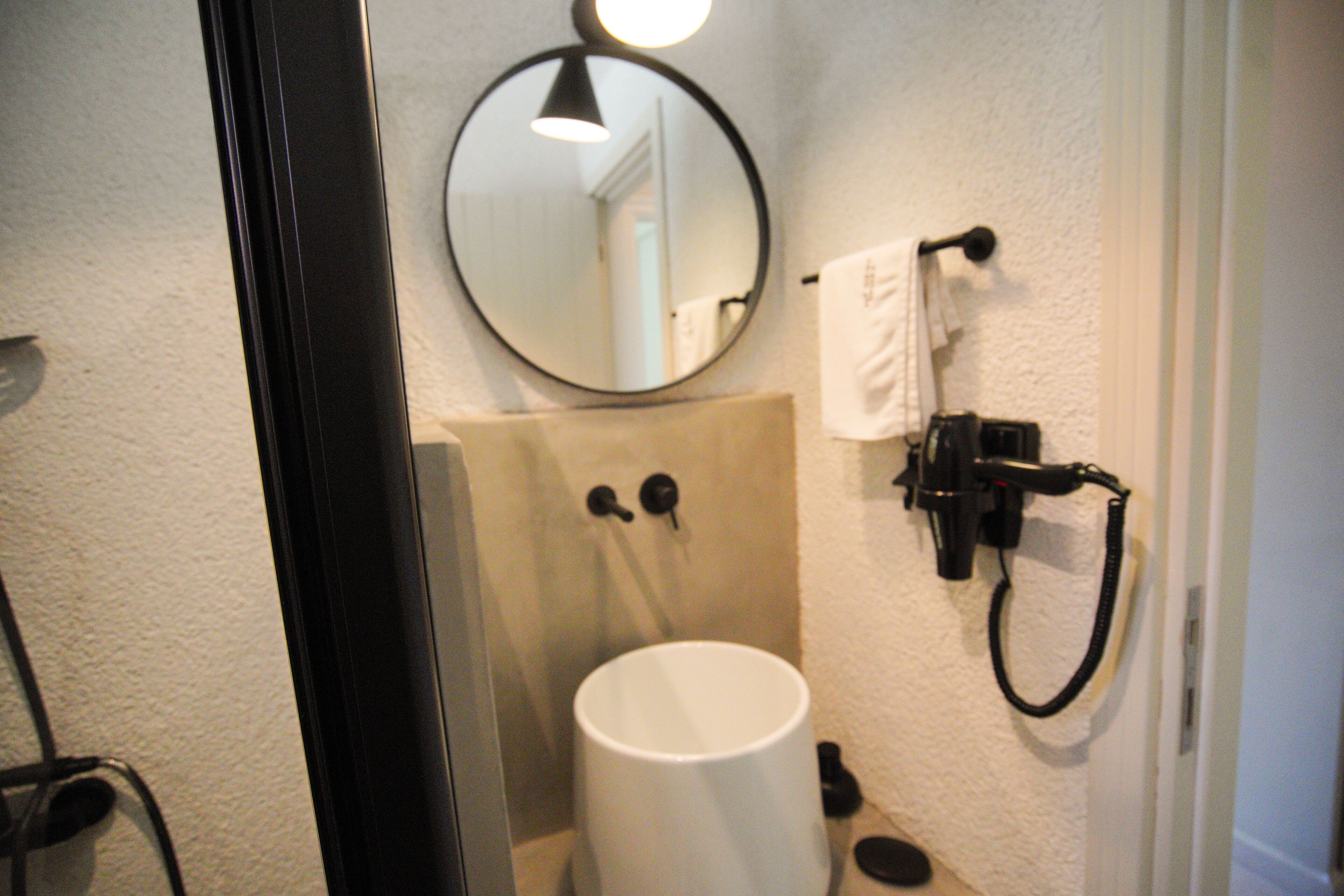 Ein Badezimmer mit rundem Spiegel, Waschbecken und Handtuchhalter.