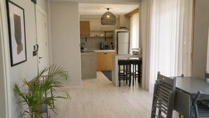 A modern kitchen with wooden cabinets, a central island, and a dining area with a table and chairs. - Alp Suites Mandalin (Ula)