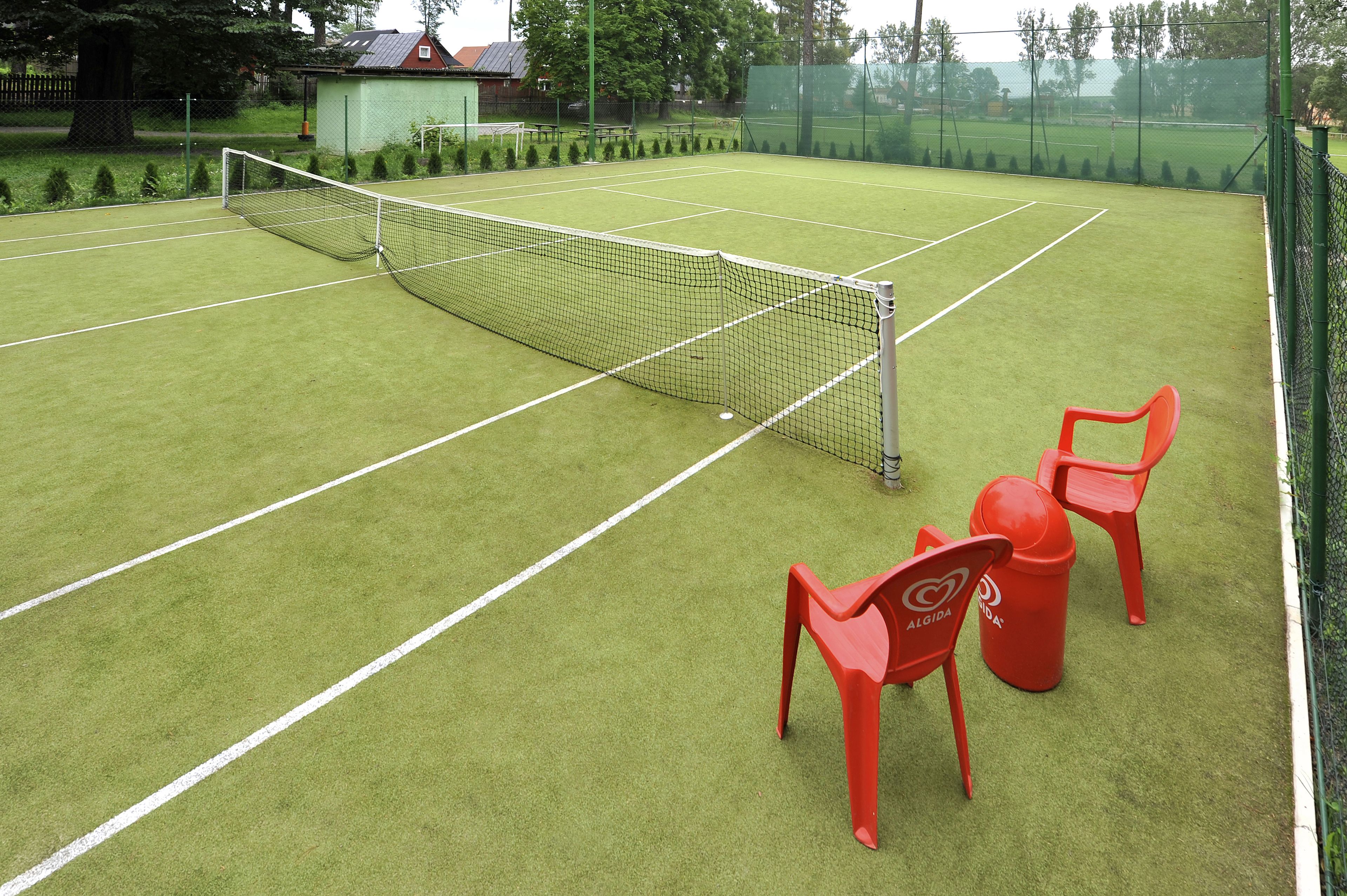 A tennis court with a net, two red chairs, and a small shed in the background.