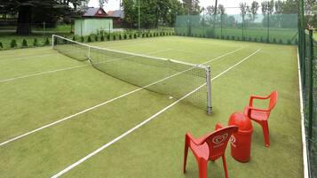 A tennis court with a net, two red chairs, and a small shed in the background.