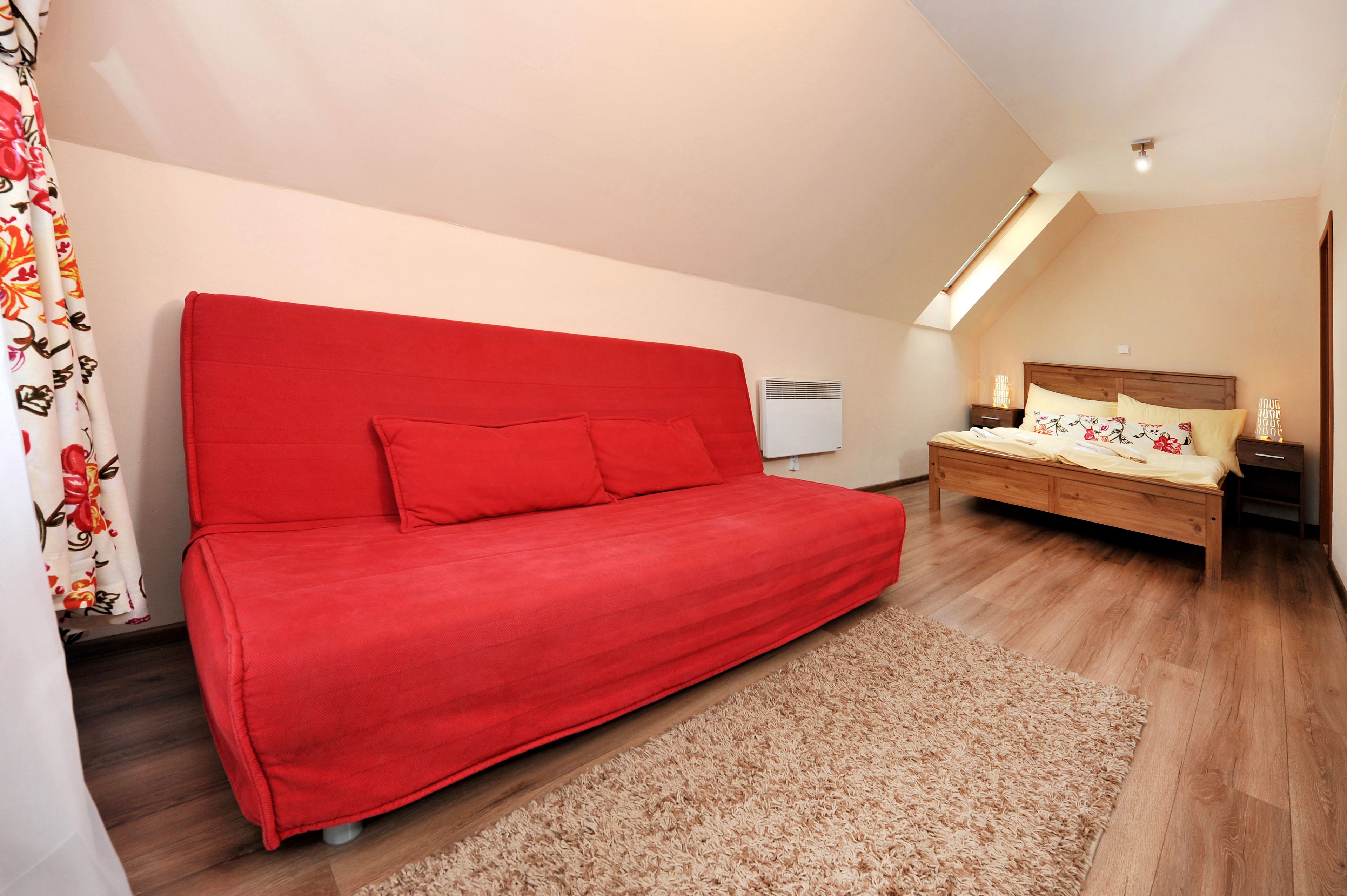 Un dormitorio con un sofá rojo, una cama de madera, un tragaluz y una pared blanca.